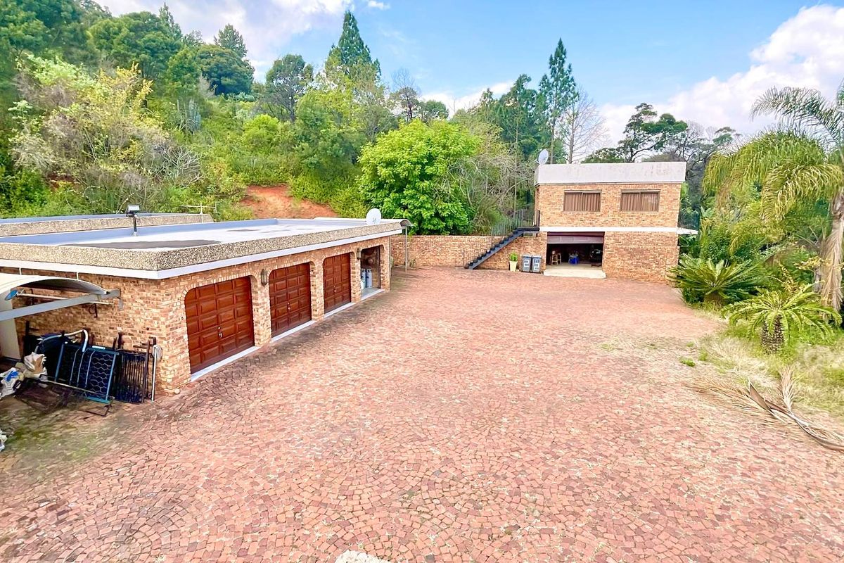 Spacious residential property featuring multiple garage bays, a paved courtyard, and a secondary structure set against a lush, sloped landscape.