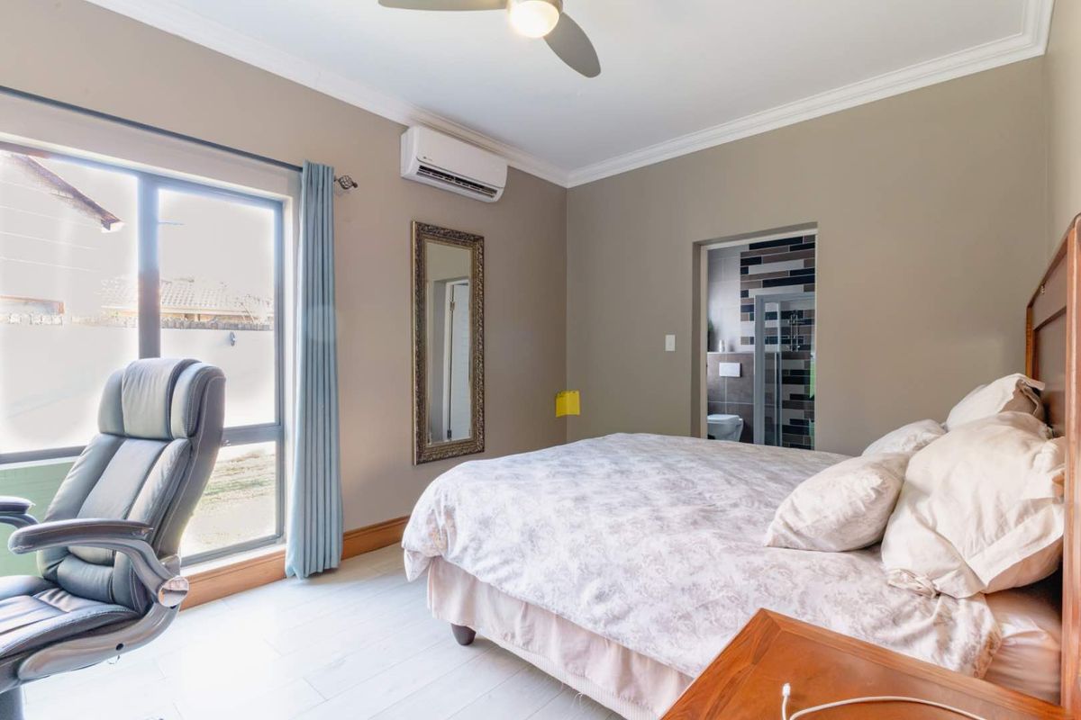 Spacious bedroom featuring an en-suite bathroom, split-system air conditioning, ceiling fan, and large windows providing natural light.