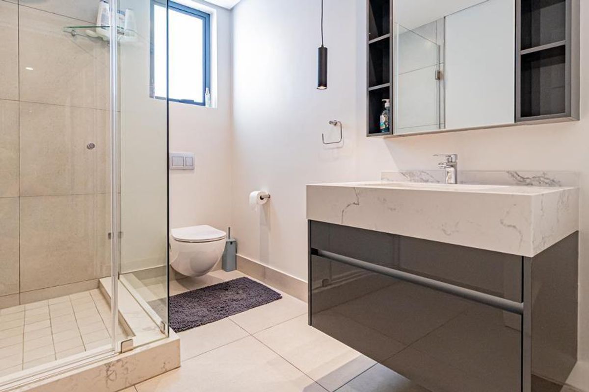Modern bathroom featuring a floating vanity with stone countertop, wall-hung toilet, and a glass-enclosed shower with neutral tiling.