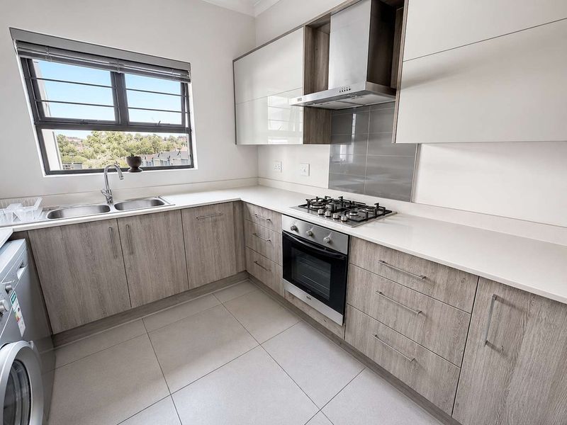 Modern kitchen featuring light wood-grain cabinetry, stone countertops, stainless steel appliances, and tiled flooring with ample natural light.