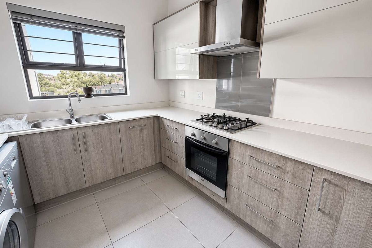Modern kitchen featuring light wood-grain cabinetry, stone countertops, stainless steel appliances, and tiled flooring with ample natural light.