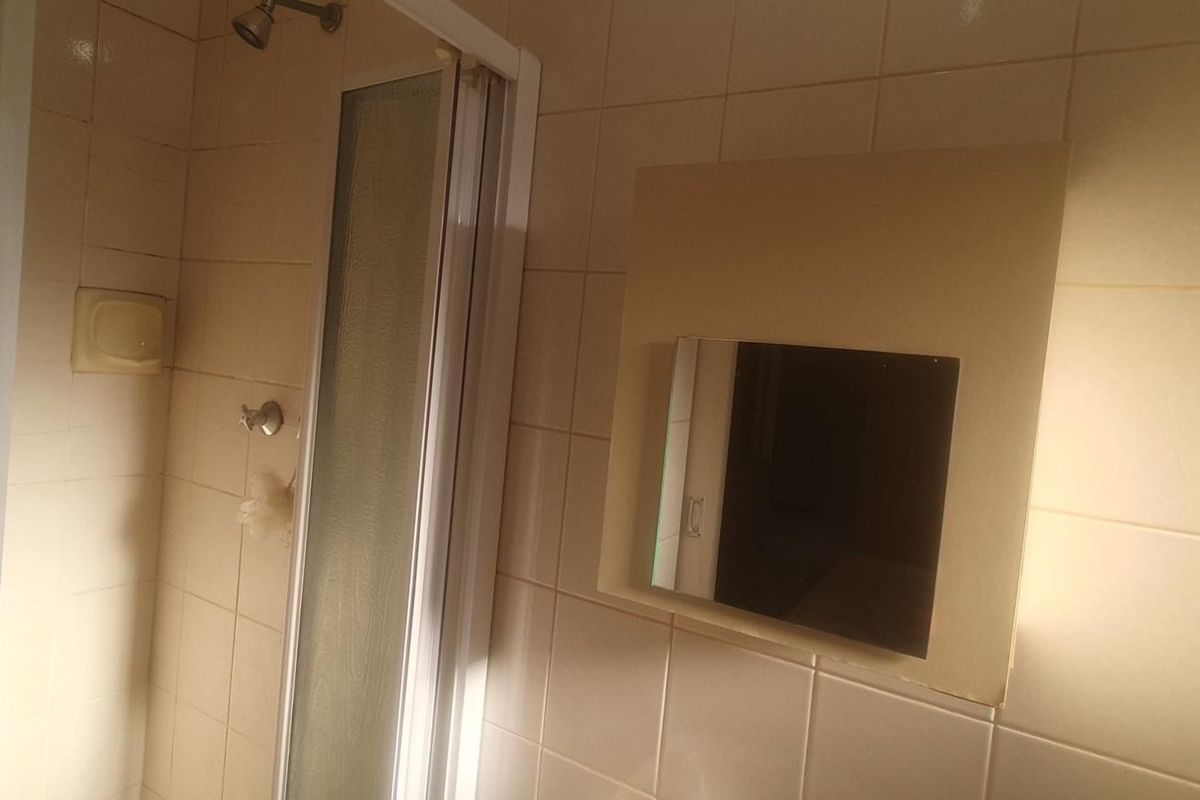 A dated bathroom featuring a shower enclosure with tiled walls and a built-in recessed medicine cabinet.