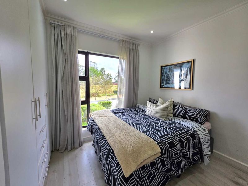 A well-maintained bedroom featuring light laminate flooring, built-in cupboards, recessed downlights, and a large window with garden views.