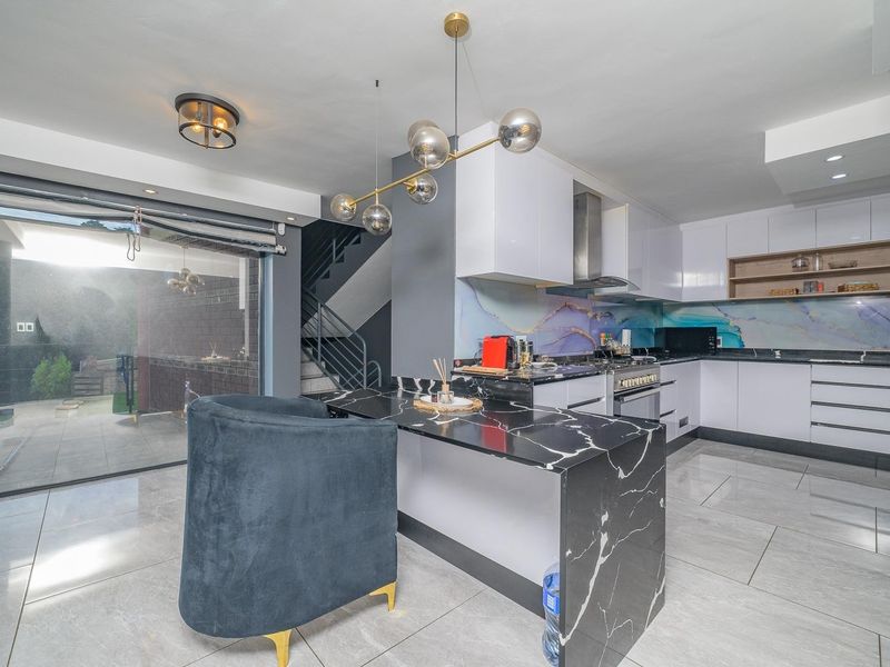 Modern kitchen featuring white gloss cabinetry, a striking marble-look waterfall island, decorative splashback, and seamless access to the outdoor patio area.