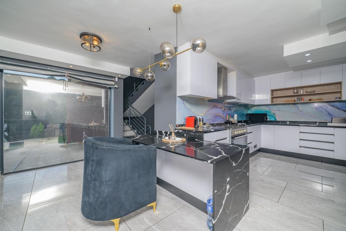 Modern kitchen featuring white gloss cabinetry, a striking marble-look waterfall island, decorative splashback, and seamless access to the outdoor patio area.