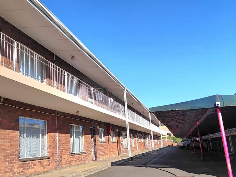 Exterior view of an apartment building featuring a brick facade, balcony access, and a covered parking area.
