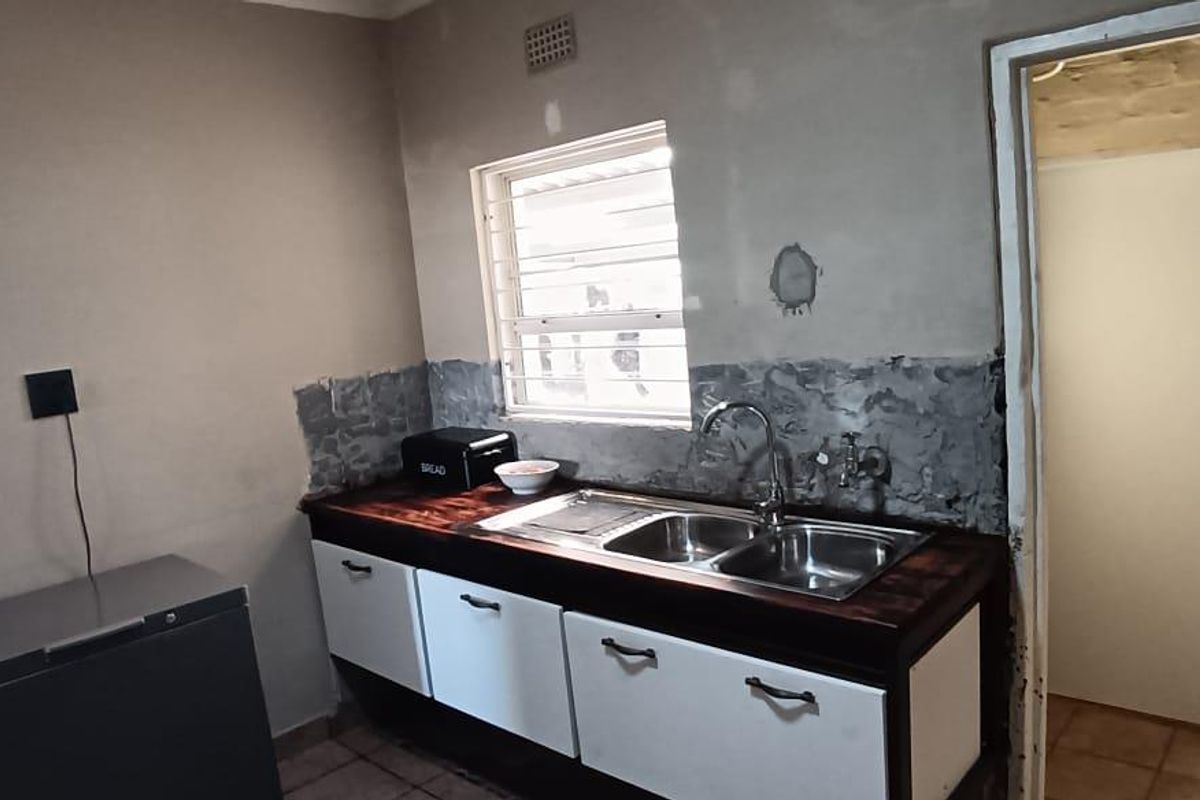 A functional kitchen area featuring a stainless steel double sink, wooden countertop, and basic cabinetry, currently requiring cosmetic renovation and wall finishing.