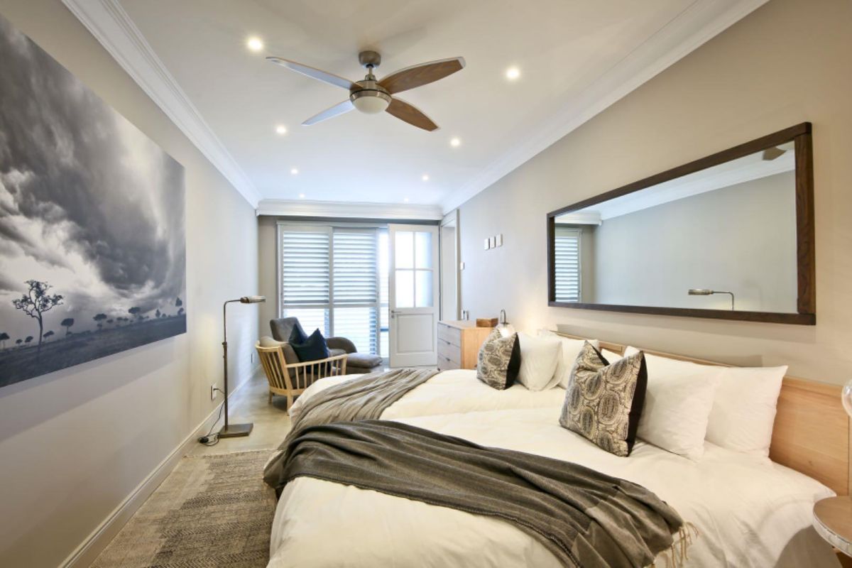 A well-appointed bedroom featuring recessed ceiling lighting, a modern ceiling fan, crown molding, and direct access to an outdoor area through a glass door.