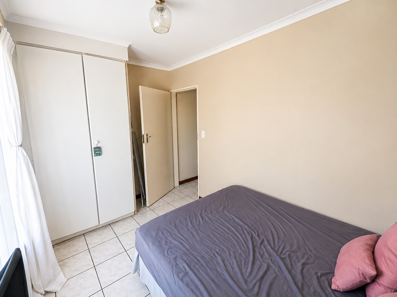 A bedroom featuring tiled flooring, built-in cupboards, and a coved ceiling, providing a functional and neutral living space.
