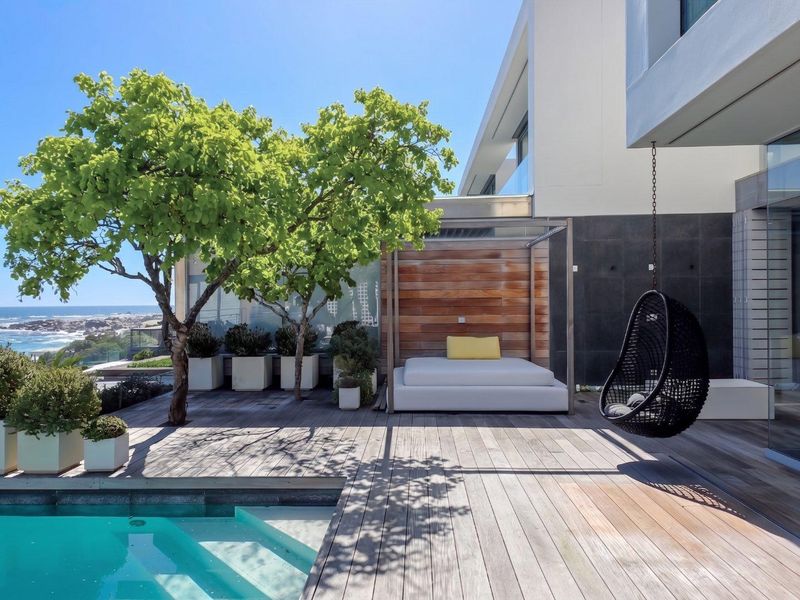 A modern outdoor pool area featuring timber decking, stone wall accents, and a glass balustrade with scenic coastal views.
