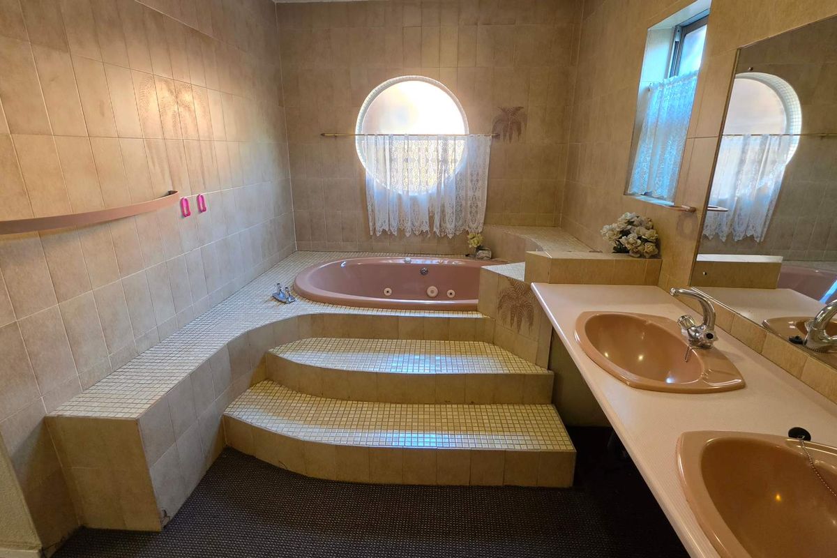 A dated bathroom featuring a sunken bathtub with tiled steps, a double vanity with integrated sinks, and a distinctive circular window.
