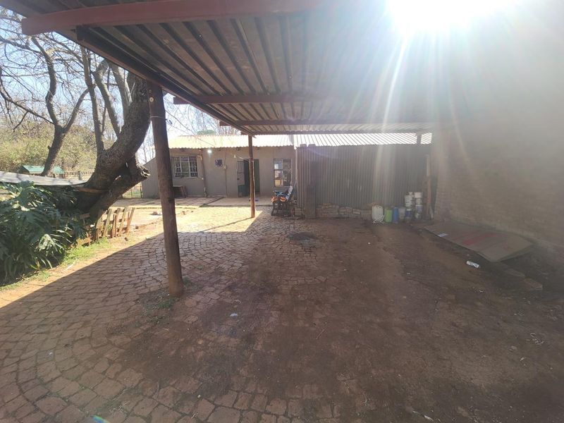 A covered outdoor patio area featuring a corrugated metal roof, timber support posts, and cobblestone paving, providing a functional space for outdoor activities.