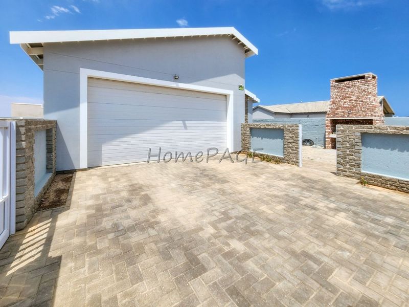 Rear exterior view featuring a paved driveway, garage access, and a built-in brick braai area with stone-clad boundary walls.