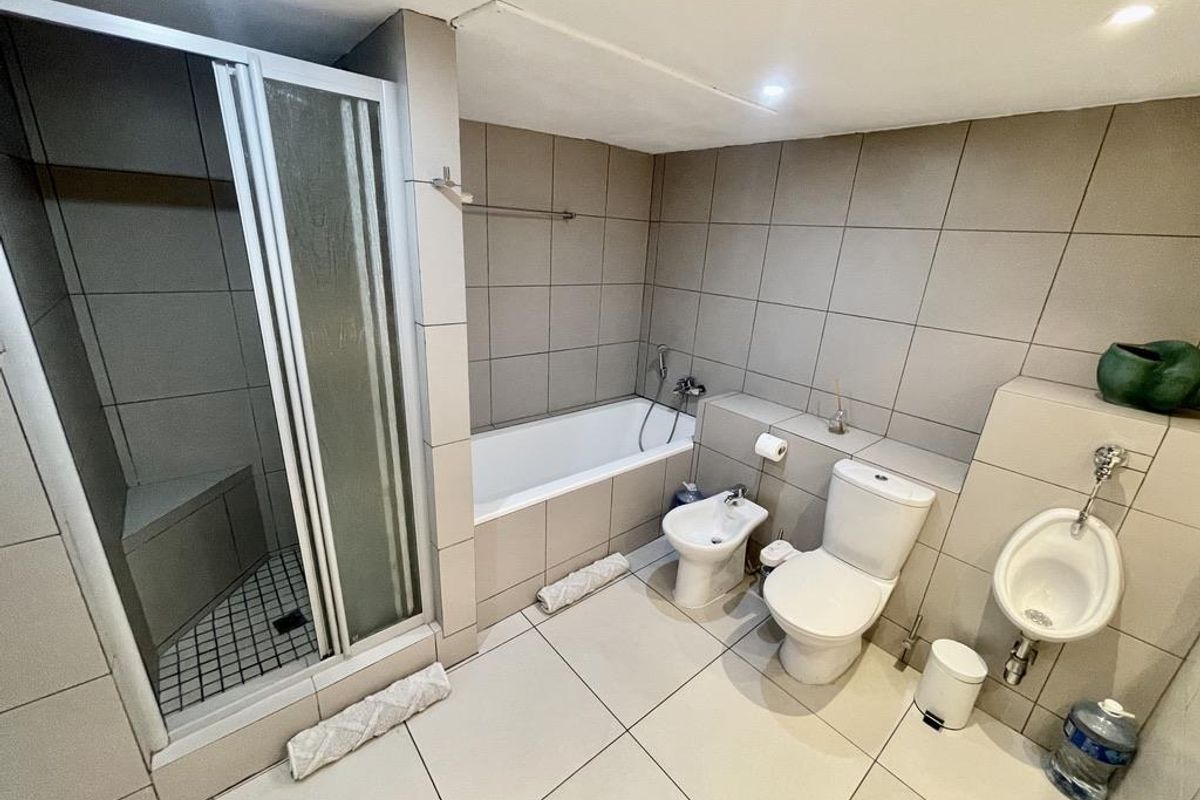 Spacious bathroom featuring a glass-enclosed shower, built-in bathtub, toilet, bidet, and wall-mounted urinal with neutral floor-to-ceiling tiling.
