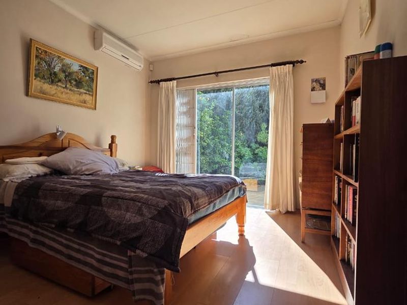 A well-lit bedroom featuring laminate flooring, a wall-mounted air conditioning unit, and sliding glass doors providing access to the garden.