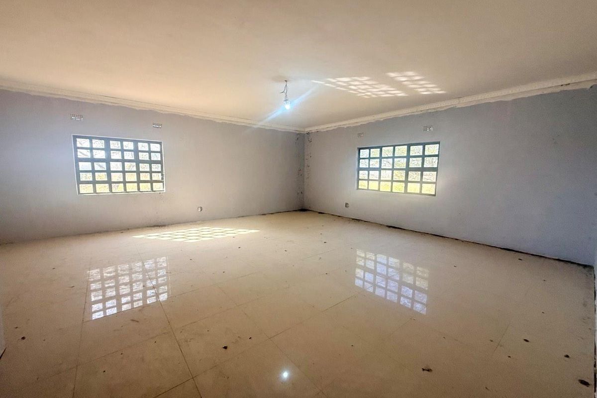 A spacious, empty living room featuring large grid-pattern windows, tiled flooring, and crown molding, providing a blank canvas for interior design.