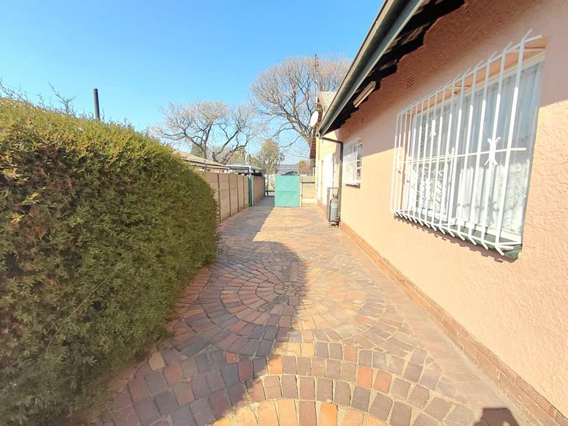 A paved side walkway along the exterior of the house, featuring security bars on the windows and a boundary wall.