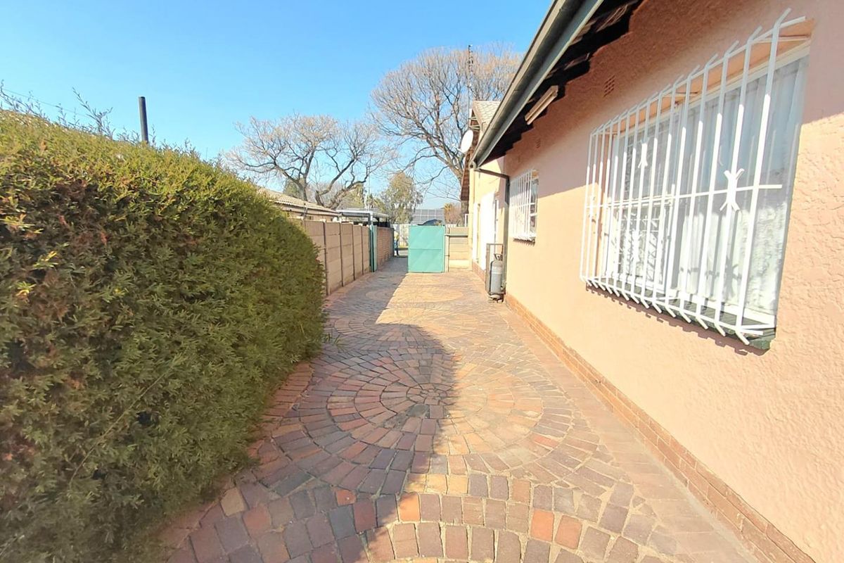A paved side walkway along the exterior of the house, featuring security bars on the windows and a boundary wall.