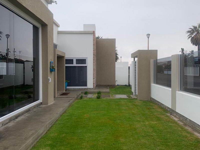A well-maintained rear garden area featuring a manicured lawn, concrete pathway, and modern boundary wall with glass balustrade detailing.