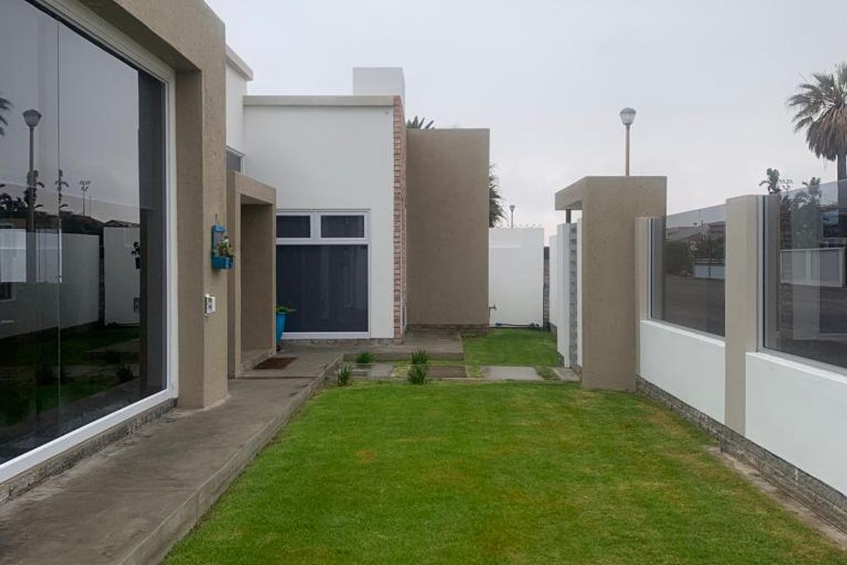 A well-maintained rear garden area featuring a manicured lawn, concrete pathway, and modern boundary wall with glass balustrade detailing.