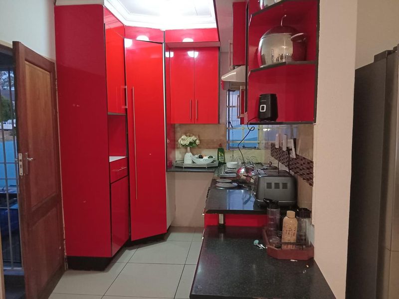 Compact kitchen featuring high-gloss red cabinetry, black granite countertops, tiled backsplash, and integrated cooking appliances.