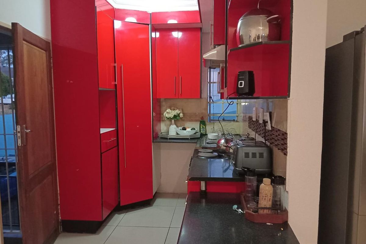 Compact kitchen featuring high-gloss red cabinetry, black granite countertops, tiled backsplash, and integrated cooking appliances.