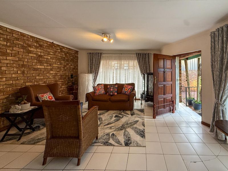 Spacious living room featuring an exposed brick wall, ceramic tiled flooring, and direct access to an outdoor patio area.