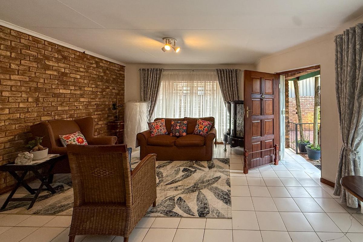 Spacious living room featuring an exposed brick wall, ceramic tiled flooring, and direct access to an outdoor patio area.