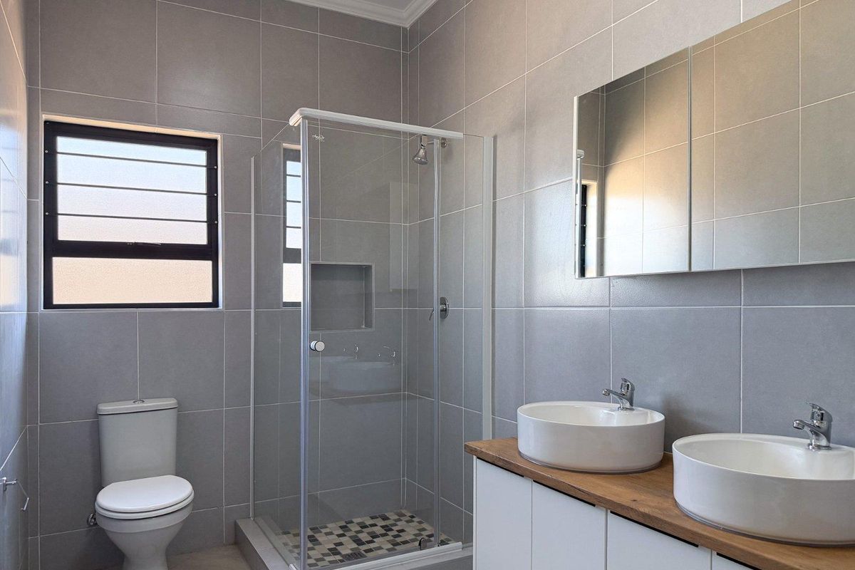 Modern bathroom featuring a double vanity with vessel sinks, a glass-enclosed shower with a built-in niche, and floor-to-ceiling grey tiling.