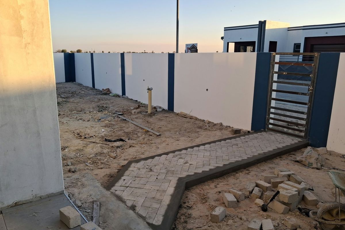 Rear yard area featuring a newly constructed boundary wall, metal gate, and paved walkway, currently awaiting final landscaping and site cleanup.