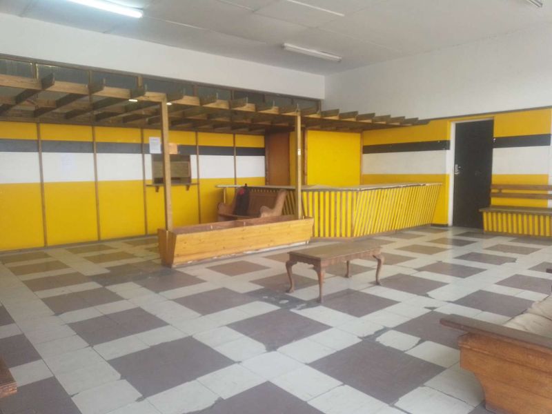 Spacious interior area featuring a built-in wooden counter, overhead pergola structure, and checkered tiled flooring, suitable for various commercial or communal uses.