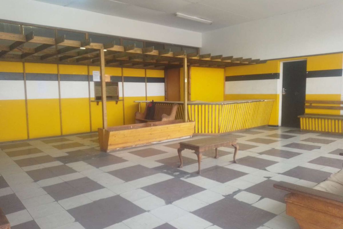 Spacious interior area featuring a built-in wooden counter, overhead pergola structure, and checkered tiled flooring, suitable for various commercial or communal uses.