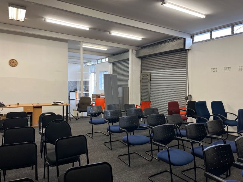 An open-plan commercial space featuring high ceilings, fluorescent lighting, and a roller shutter door, suitable for office or workshop use.