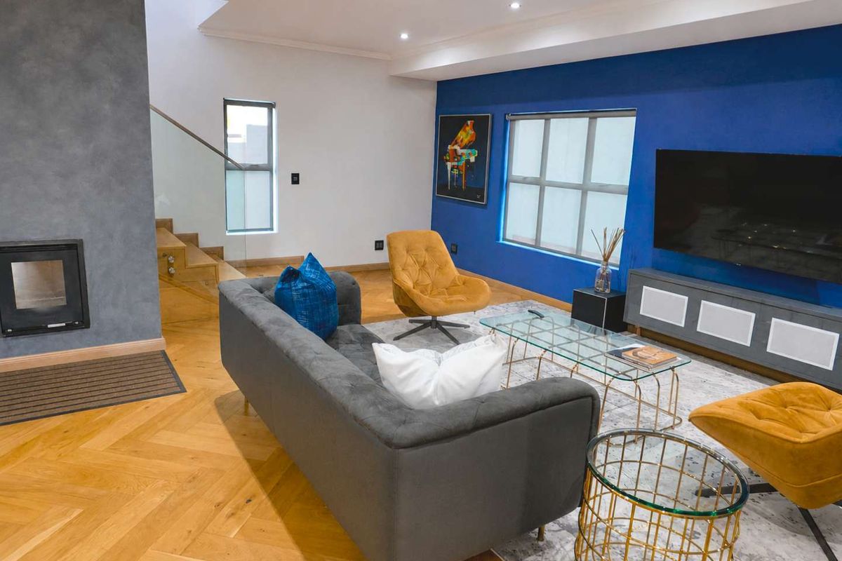 Modern living room featuring herringbone wood flooring, a built-in fireplace, and a striking blue accent wall with an adjacent glass balustrade staircase.