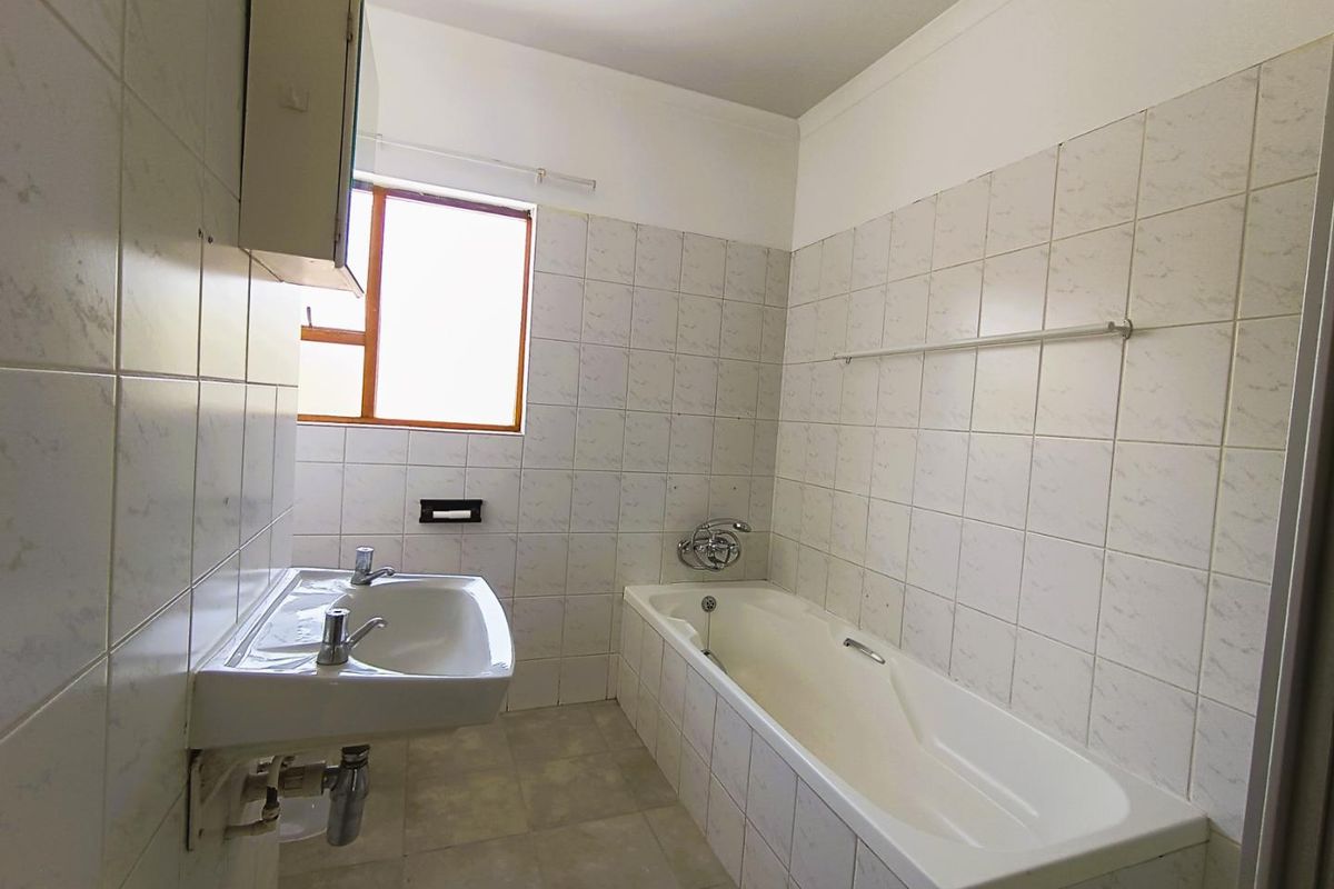 A functional bathroom featuring a built-in bathtub, wall-mounted basin, and tiled finishes throughout.