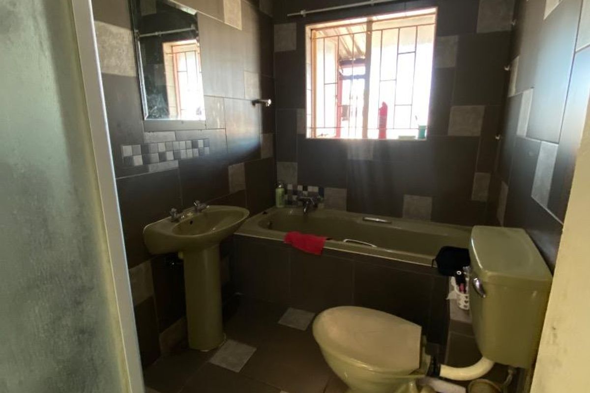 A dated bathroom featuring a pedestal basin, bathtub, and toilet with dark wall and floor tiling and security bars on the window.