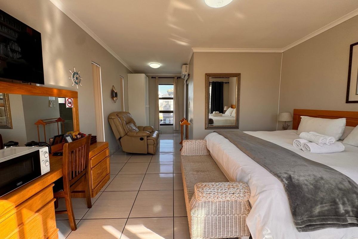 A spacious bedroom featuring tiled flooring, a wall-mounted air conditioning unit, and a window providing natural light.