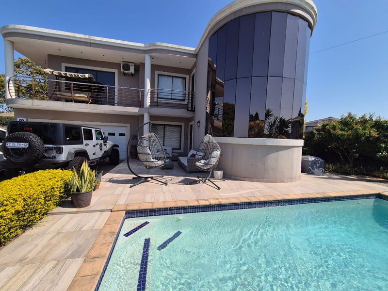 A modern two-story home exterior featuring a swimming pool, tiled patio area, and a distinctive curved glass architectural feature.