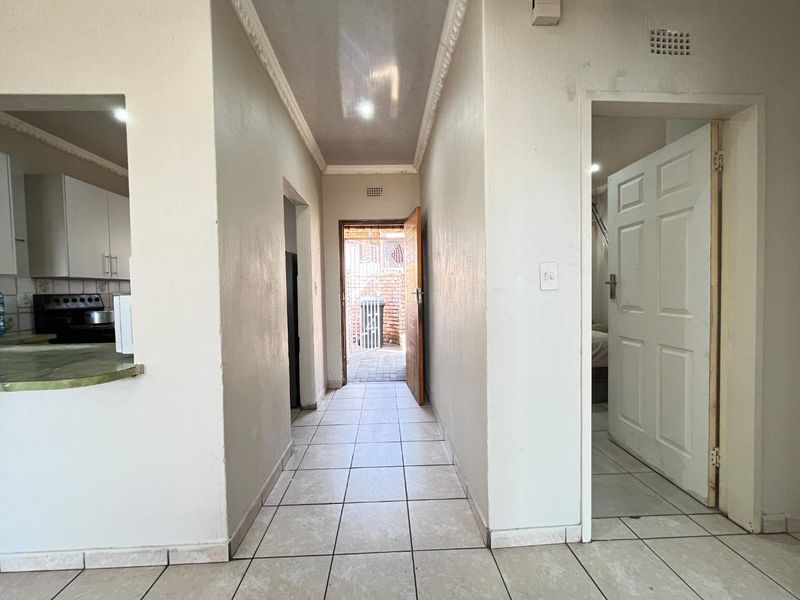 A tiled hallway connecting the kitchen and other rooms, featuring coved ceilings and access to an exterior rear area.