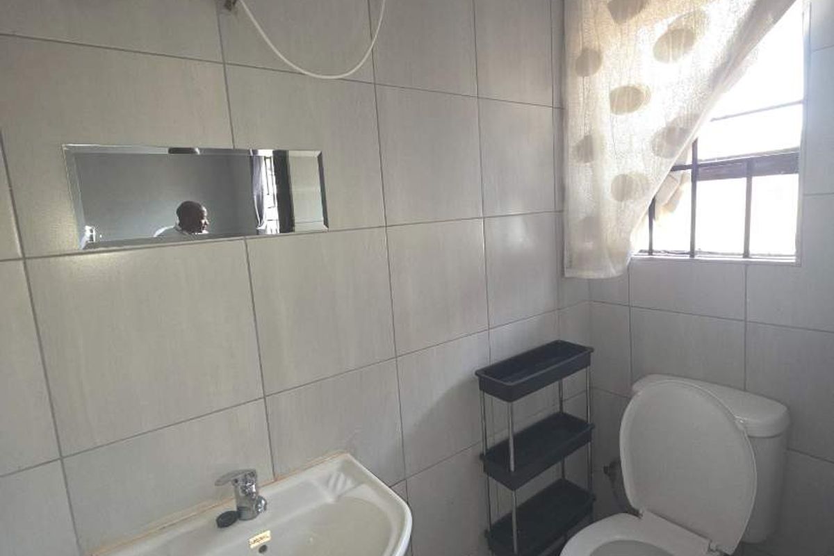 A compact bathroom featuring tiled walls and floors, a pedestal basin, and a toilet, with visible exposed plumbing and electrical wiring.