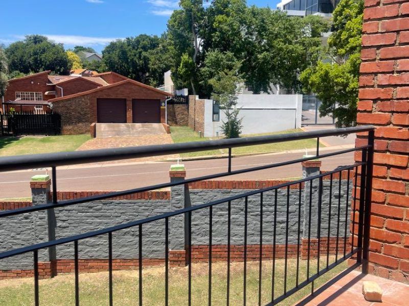 A private balcony featuring tiled flooring and a metal balustrade, offering an elevated view of the surrounding neighborhood and street.