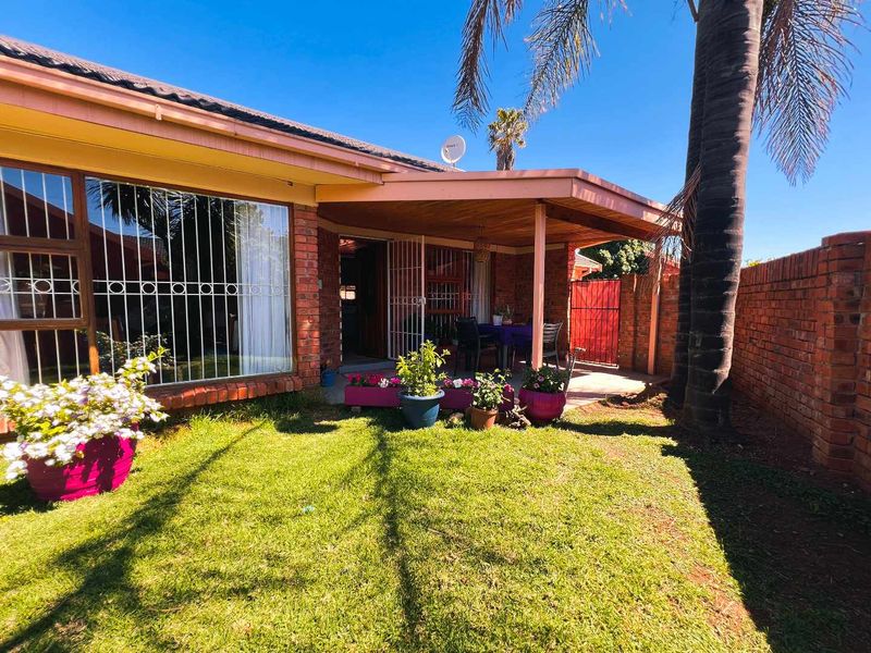 A rear view of the townhouse featuring a covered patio area, brick boundary wall, and a small garden space.