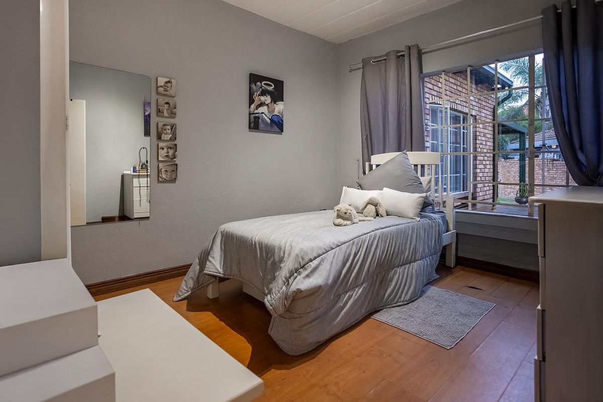 A bedroom featuring wood-look flooring, a large window with security bars, and a wall-mounted mirror.