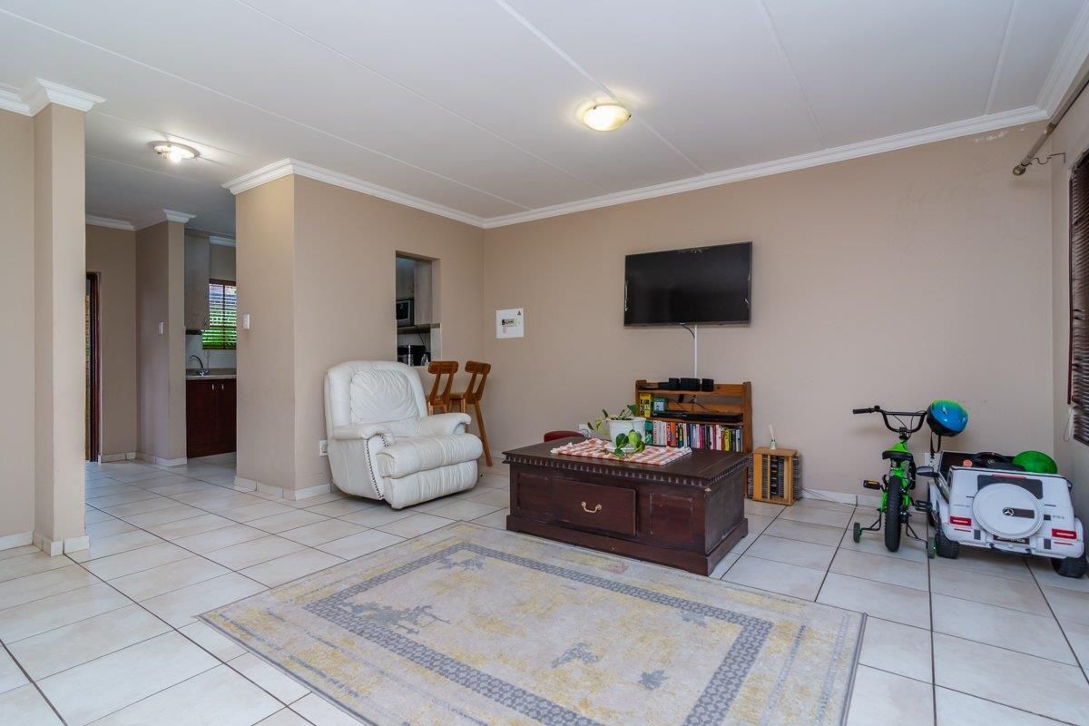 A spacious living area featuring neutral wall tones, tiled flooring, and a convenient pass-through window connecting to the kitchen area.