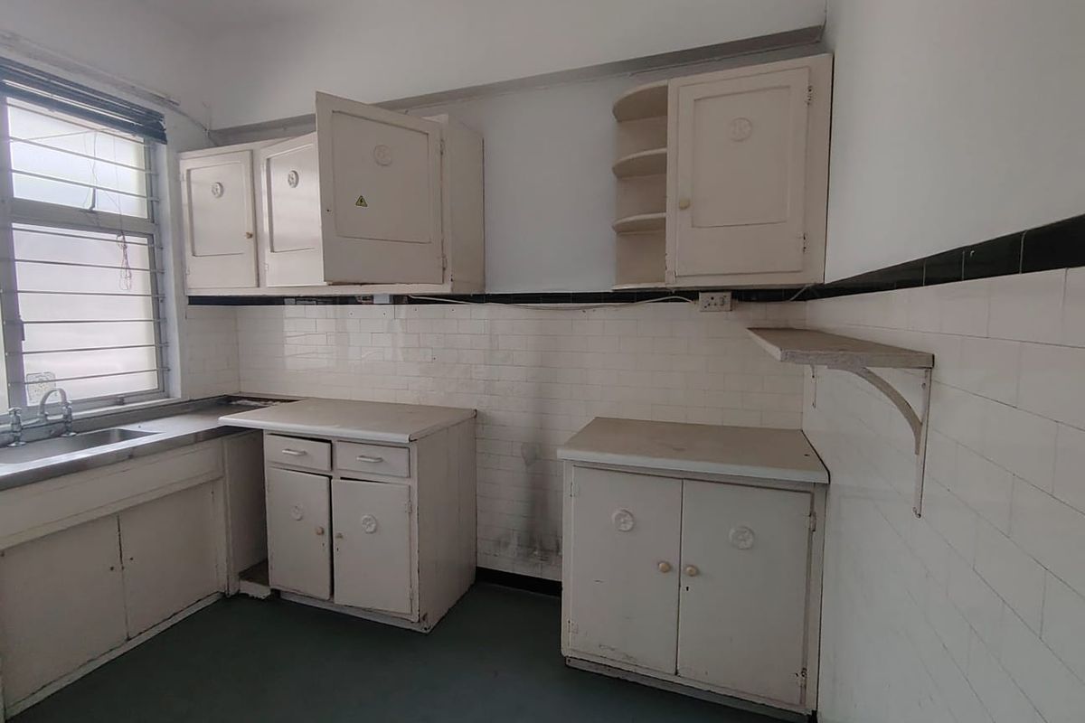 A dated office kitchenette featuring original built-in cabinetry, tiled splashbacks, and a stainless steel sink unit with a window view.