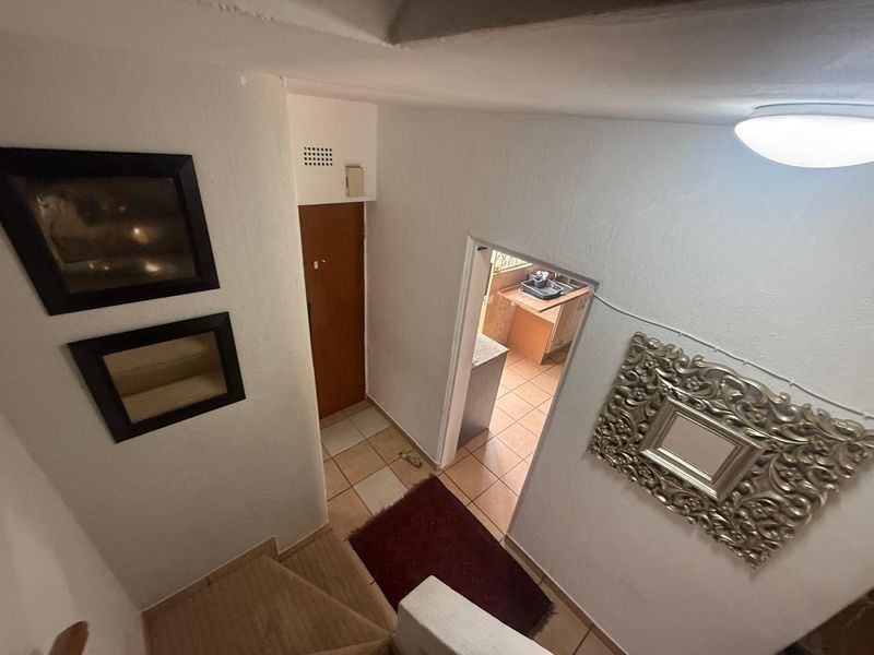 A view from the top of a staircase looking down into a hallway with tiled flooring and access to an adjacent kitchen area.