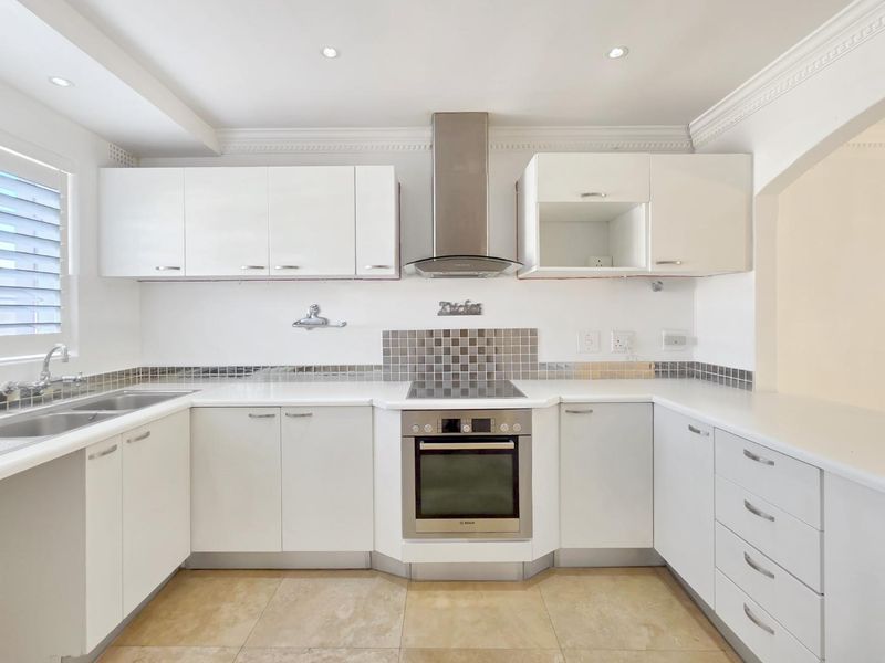 A clean, modern kitchen featuring white cabinetry, stainless steel appliances, stone countertops, and a tiled splashback with recessed lighting.