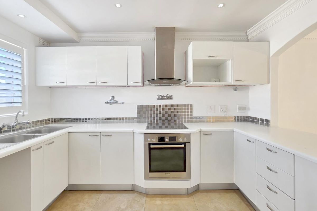 A clean, modern kitchen featuring white cabinetry, stainless steel appliances, stone countertops, and a tiled splashback with recessed lighting.