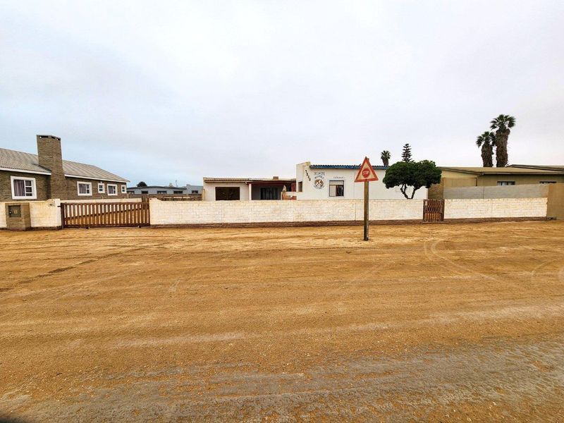 Street view of the property frontage featuring a perimeter wall, gated access, and an unpaved road approach.