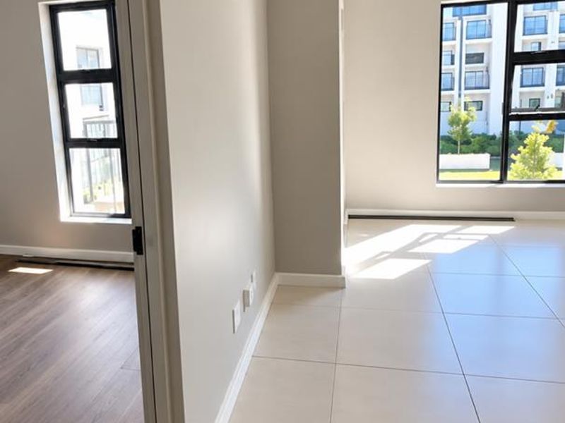 Bright and modern open-plan living area featuring neutral tiled floors, clean finishes, and large windows allowing for ample natural light.